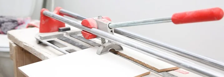 Ein Fliesenschneider mit einem roten Griff schneidet eine Fliese